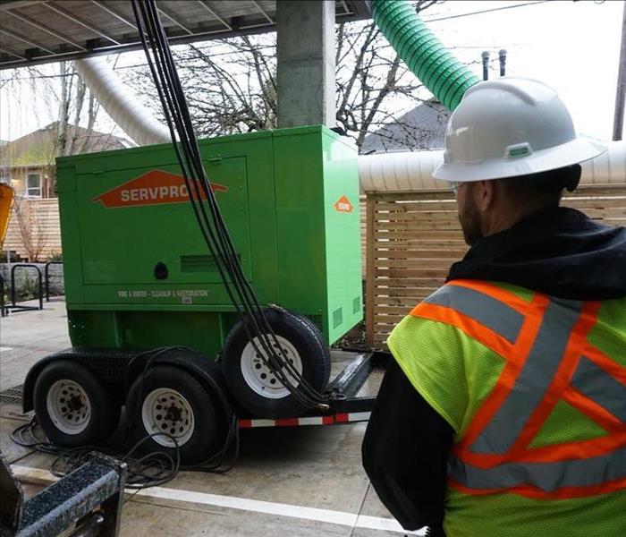 SERVPRO employee in PPE stands next to SERVPRO green generator
